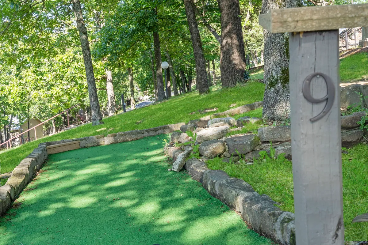 A cheerful view of the mini-golf course with a green putting surface, stone borders, and a numbered post, surrounded by greenery. The area exudes a playful vibe, inviting guests to enjoy friendly mini-golf competitions and social outdoor activities.