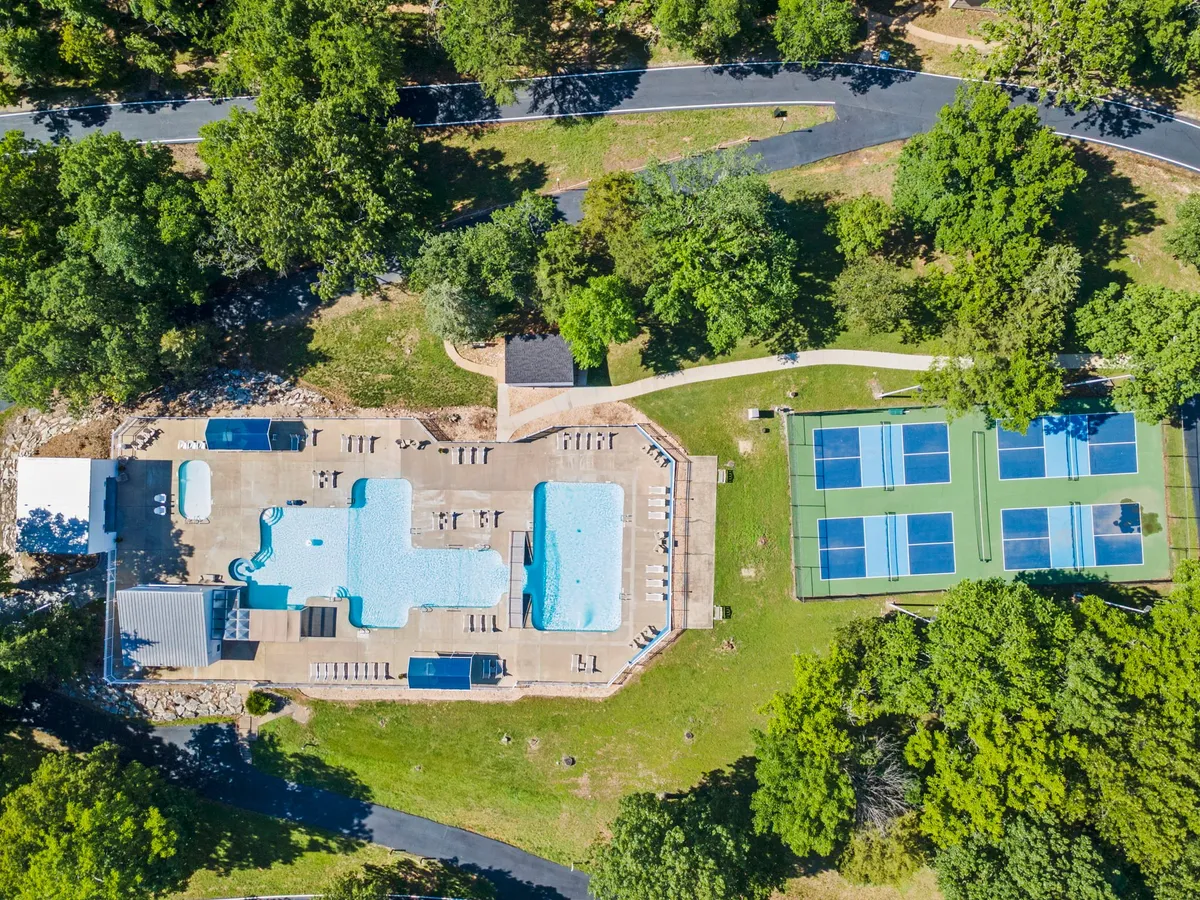 This exterior image features a vibrant resort area with swimming pools, tennis courts, lounge chairs, and lush surrounding greenery. The scene is full of activity, highlighting both relaxation and recreation with guests swimming, sunbathing, and socializing around the amenities.