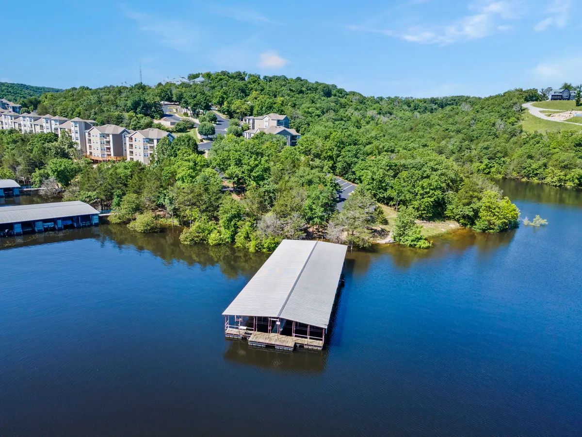 A peaceful view of the community dock extending out onto the lake, surrounded by greenery and with residential buildings in the background. The setting is quiet and inviting, suggesting both adventure and moments of calm by the water.