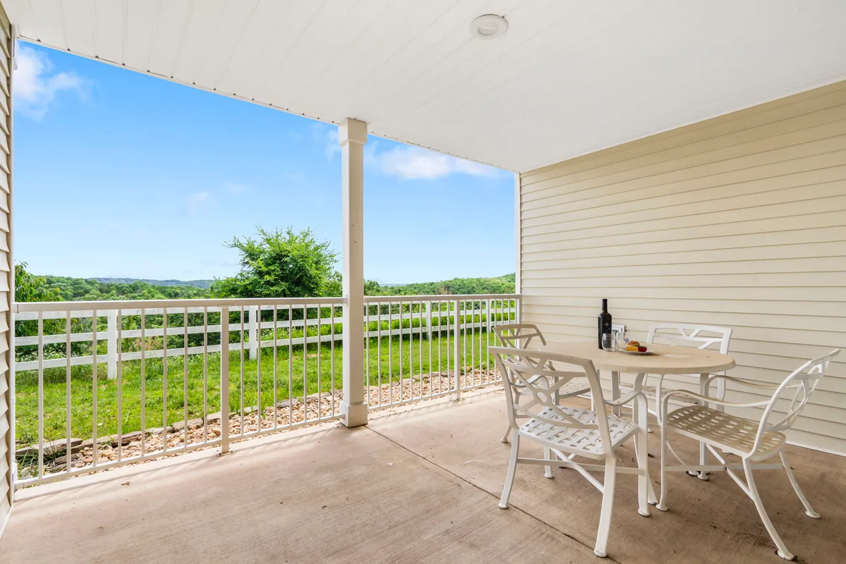 An outdoor deck area with a table and chairs set up for al fresco dining, a bottle of wine, snack plate, and an expansive view of the landscape. The lighting suggests a peaceful time of day, underscoring the space as a perfect nook for relaxation or sharing special moments.