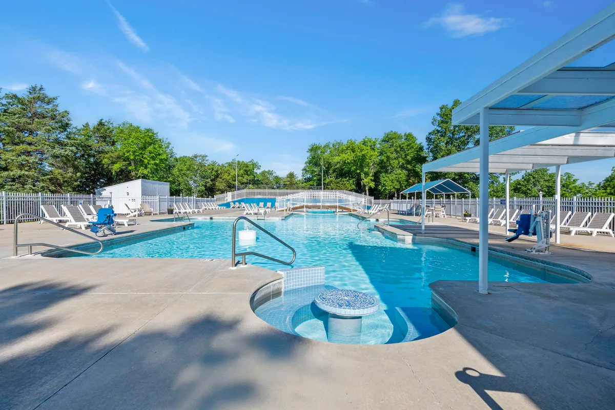 A sparkling outdoor swimming pool with a hot tub is surrounded by sun loungers and lush greenery. The area exudes a leisurely vibe, ideal for family gatherings, sunbathing, or relaxing swims. The landscape hints at the resort’s scenic, refreshing atmosphere.