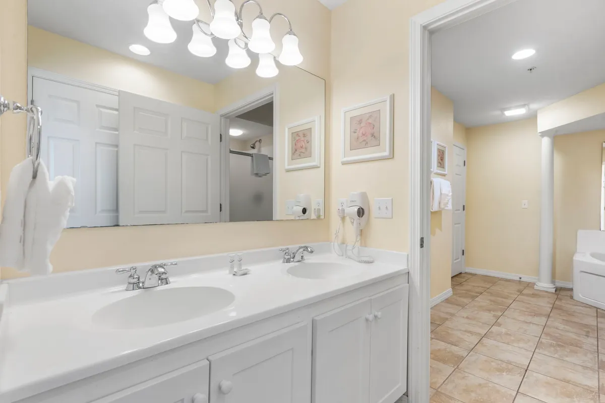 A cheerful and modern bathroom with a double sink, large mirror, framed floral art, and quality lighting. The space is fresh and functional, perfect for morning routines or winding down with a relaxing bath.
