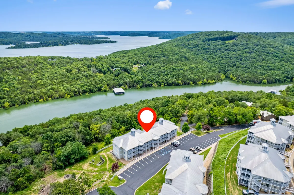 A broad view captures a winding river bordered by green hills, with distant buildings and a parking lot visible. The setting exudes tranquility and offers a clear sense of the natural environment surrounding the property.