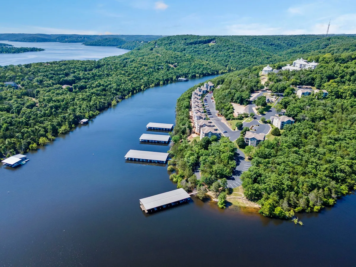 A picturesque view of Table Rock Lake winding past a cluster of homes and boathouses, framed by lush greenery. The water reflects the sky, evoking a tranquil, adventurous lakeside atmosphere ideal for boating, fishing, or simply taking in the scenery.