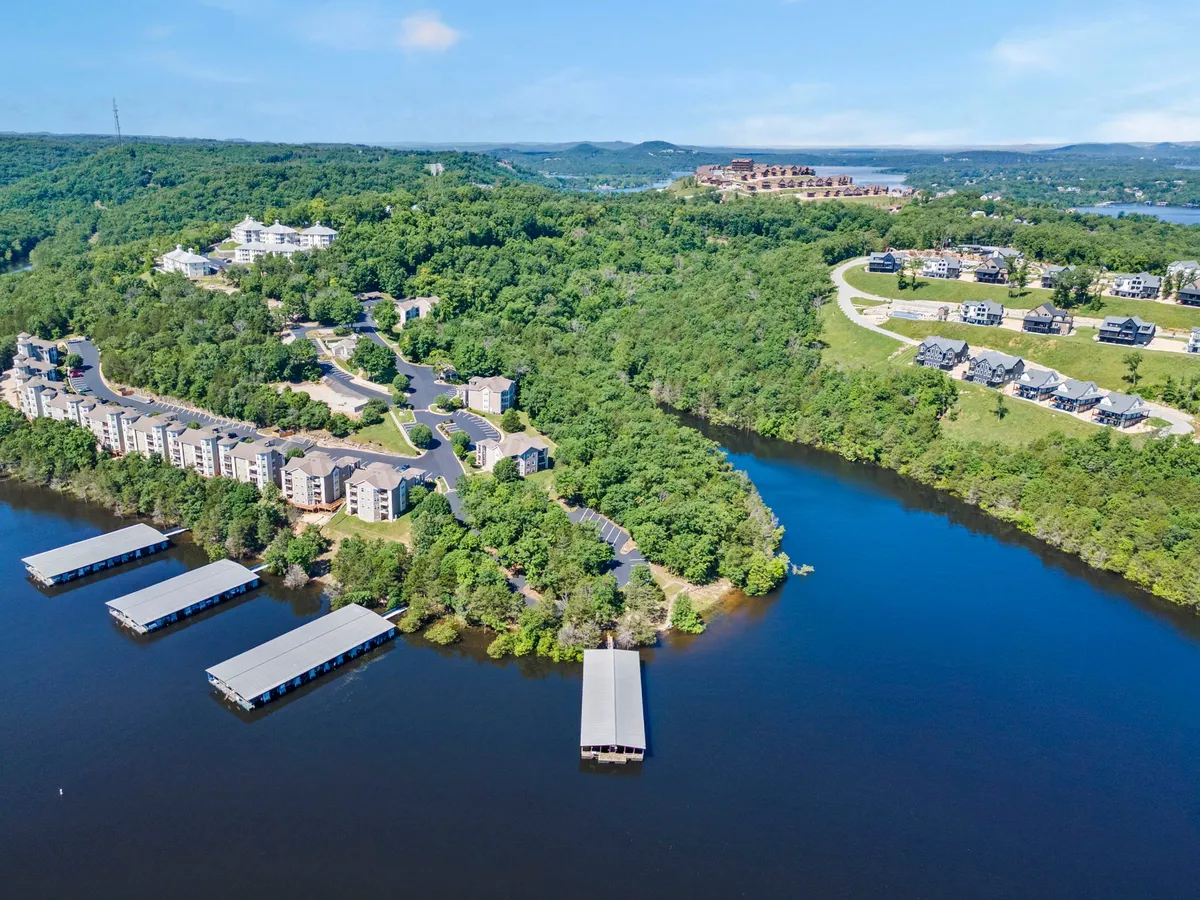 This exterior shot showcases waterfront properties, communal docks, lush greenery, and gently rolling hills. The setting features easy access to the water and visible walking paths, ideal for both humans and pets to roam and explore.