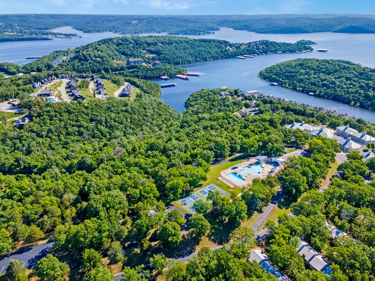 An exterior overview showing the resort's swimming pools, tennis courts, panoramic lake views, and lush green surroundings. The image highlights the range of recreational amenities available to guests.