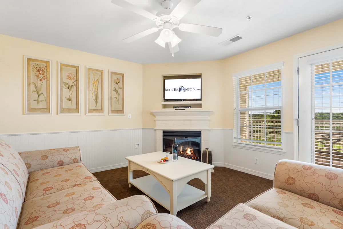 A cozy living room scene featuring a plush sofa, coffee table, inviting fireplace, and wall art. The space feels homey and perfect for family relaxation, game nights, or unwinding by the fire, with a television also visible for entertainment.