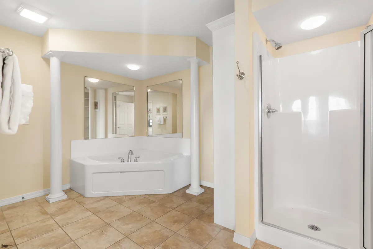 A luxurious ensuite bathroom with a jacuzzi tub, mirrors, and elegant columns. The space is bright and inviting, designed for relaxation and self-care rituals, providing a spa-like experience.